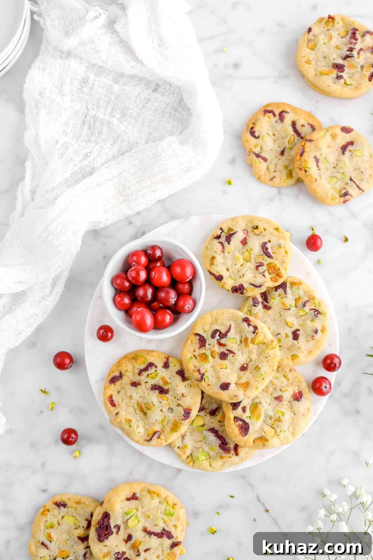 Cranberry Pistachio Slice-and-Bake Cookie Recipe 15 cookies on marble with bowl of fresh cranberries, white cheese cloth, and flowers