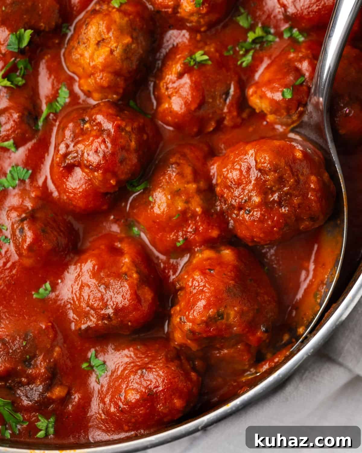 A spoon scooping a serving of gluten free meatballs from a saucepan.