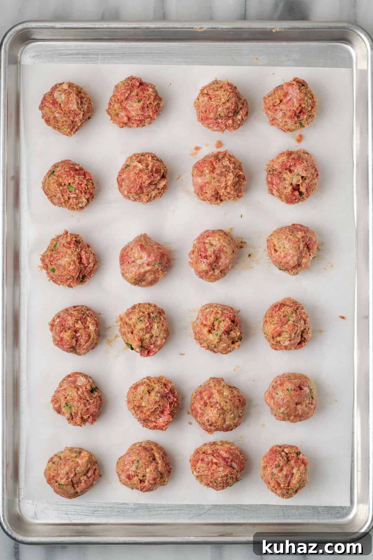 Uncooked meatballs laid out on a baking sheet. 