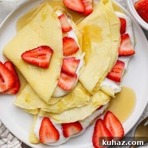 Tiramisu Crepe Roll with Cottage Cheese 6 Crepes folded and topped with sliced strawberries, cream, and syrup on a white plate.