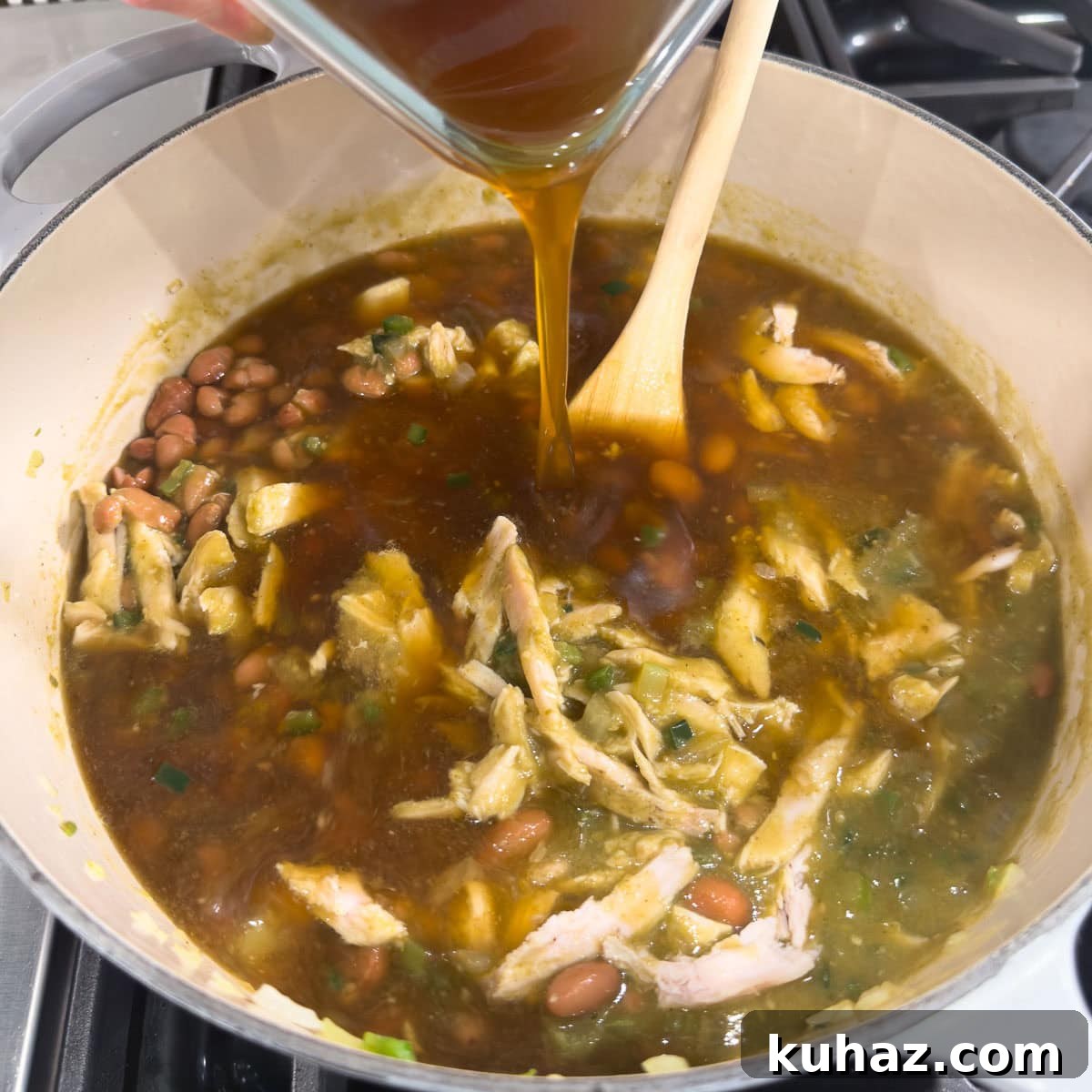 Zesty Tomatillo Soup Recipe with Chicken or Turkey 9 Deep brown turkey broth pouring into a soup pot of soup with a wooden spoon in the back.