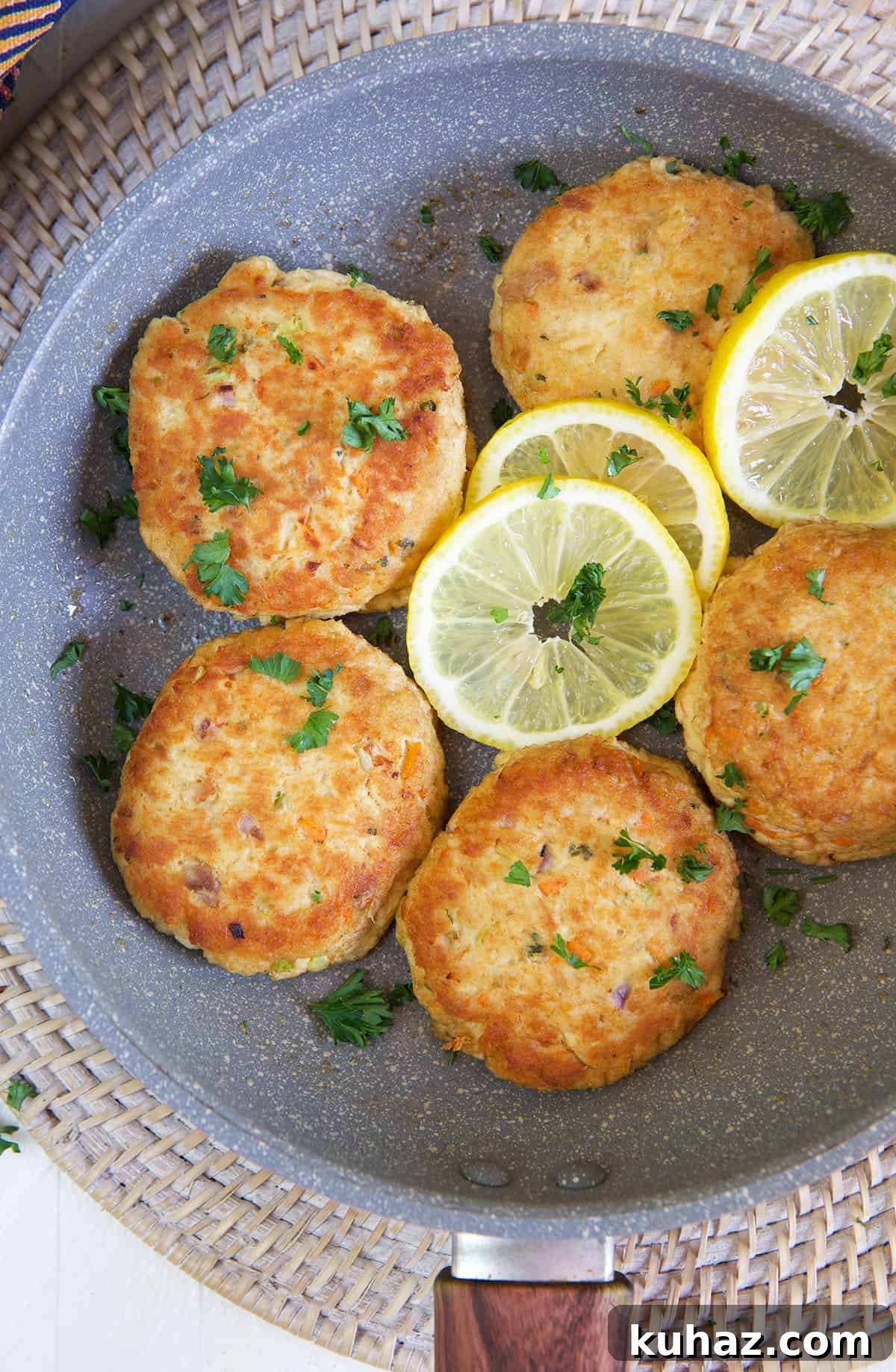Tuna patties are arranged in a large skillet with lemon slices.