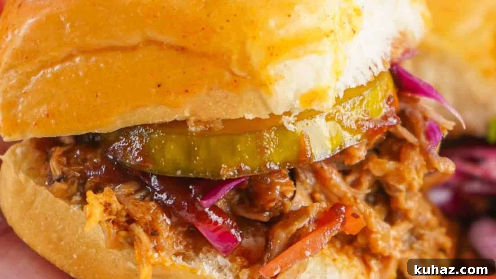 19 BBQ Dinner Recipes That Made Dad Stop Asking What's Next 15 Close-up of a pulled pork sandwich with pickles and red cabbage on a bun, held in hand, with chips in the background.
