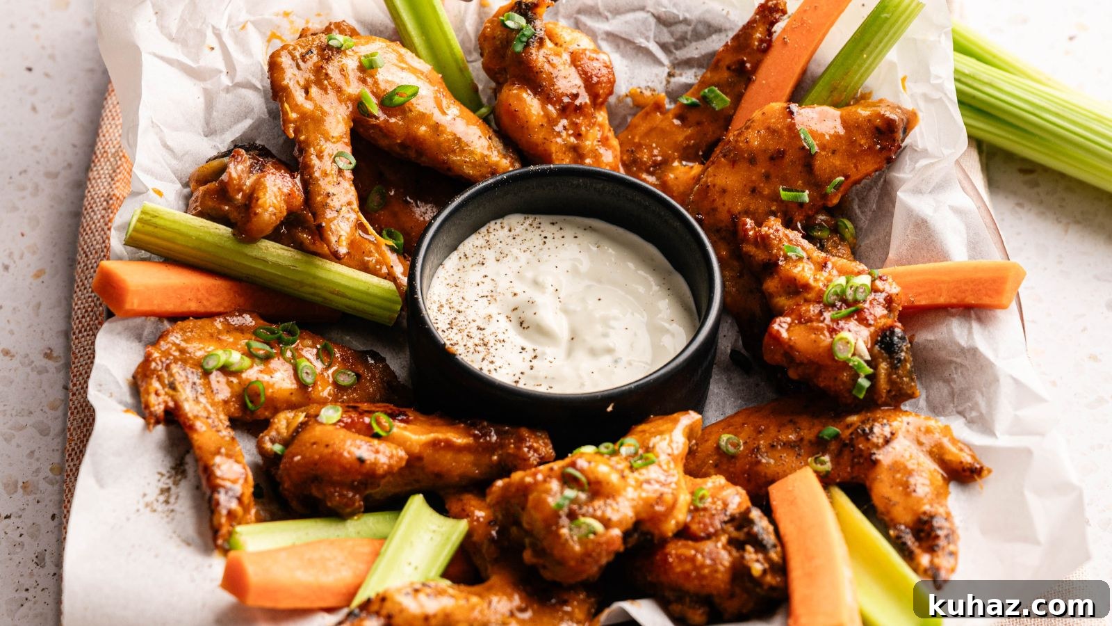 19 BBQ Dinner Recipes That Made Dad Stop Asking What's Next 10 A tray of sauced chicken wings garnished with chopped green onions, served with celery and carrot sticks, and a cup of creamy dipping sauce in the center.