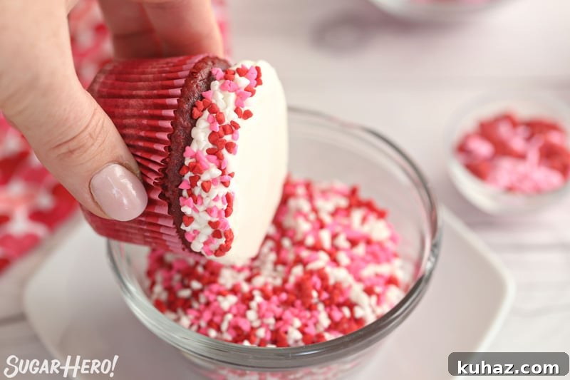 Hand dipping the edges of a frosted cupcake in heart-shaped sprinkles