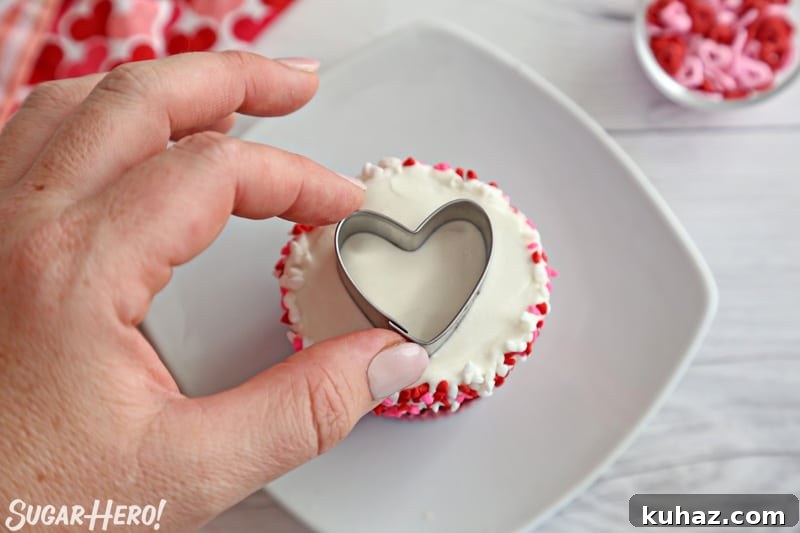 Placing a small heart-shaped cookie cutter on top of a cupcake