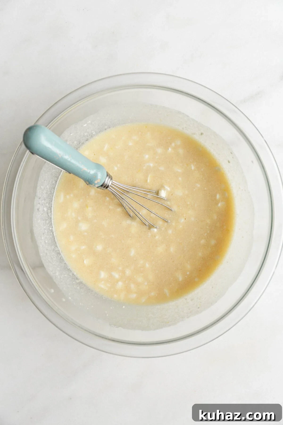 wet ingredients to make blueberry cottage cheese muffins mixed up in a mixing bowl with a blue whisk.