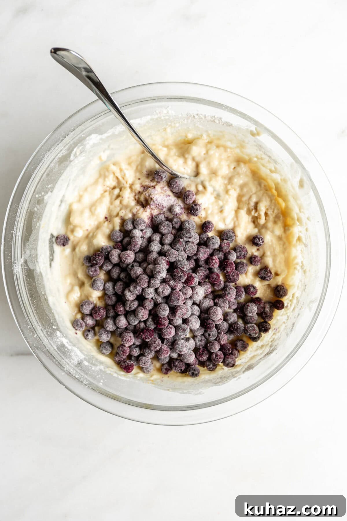 blueberry muffin batter with a pile of blueberries in a clear mixing bowl.