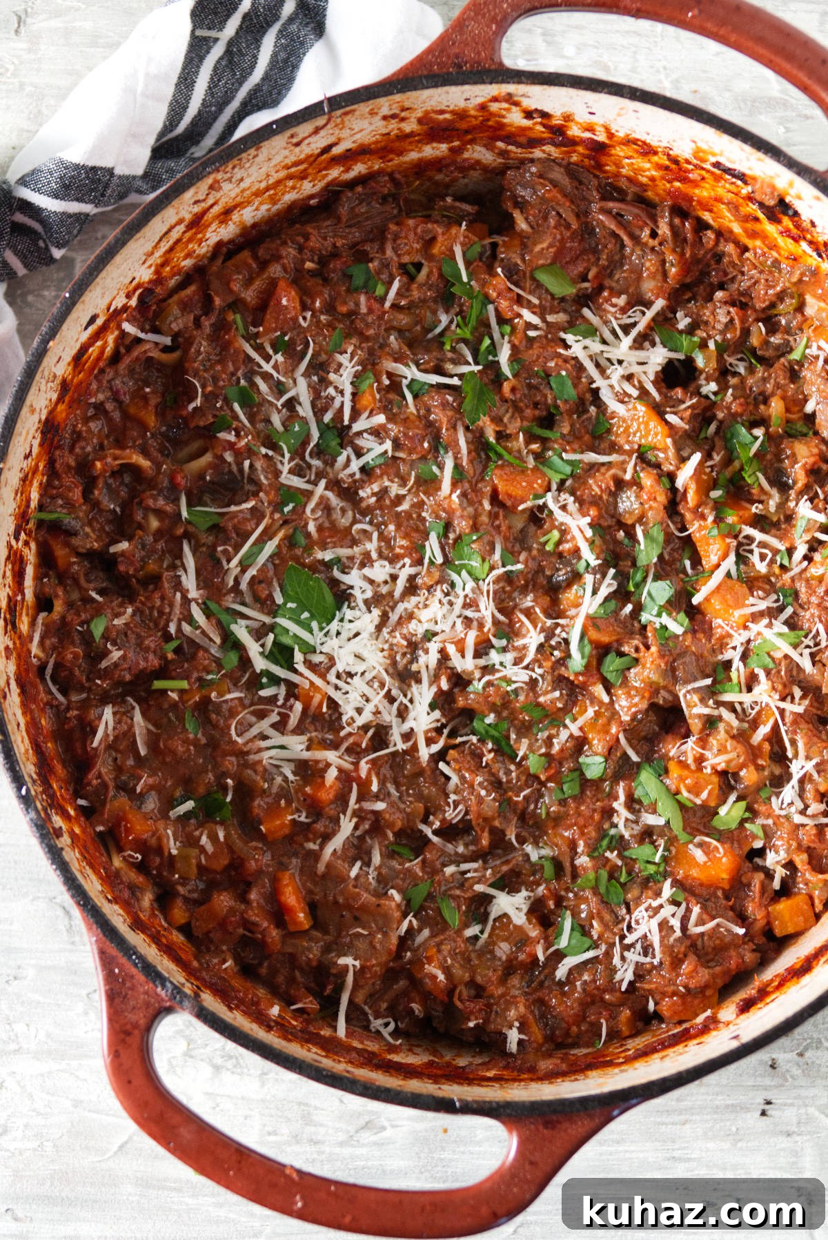 short rib ragu sauce in a dutch oven finished with parsley and grated parmesan
