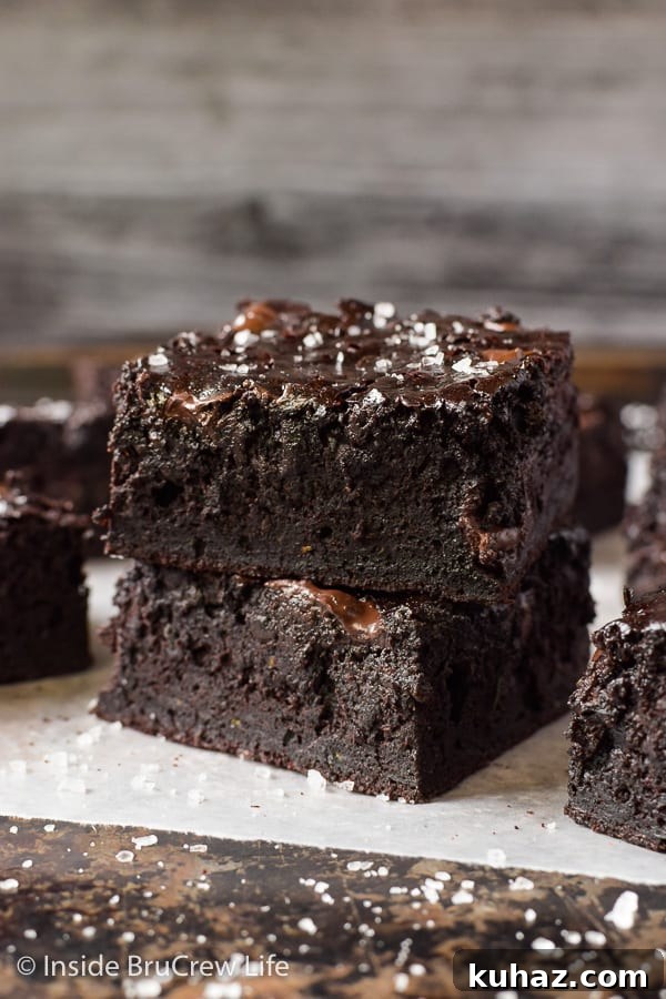 Fudgy Dark Chocolate Zucchini Brownies - these rich dark chocolate brownies have dark chocolate chips and shredded zucchini in them. Make this amazing recipe with the extra veggies from your garden. Two chocolate zucchini brownies stack on top of each other and sprinkled with sea salt