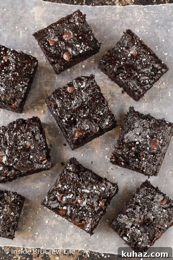 Fudgy Dark Chocolate Zucchini Brownies - dark chocolate chips and sea salt add a sweet and salty flair to these fudgy zucchini brownies. Try this recipe with your extra zucchinis. Overhead picture of 8 chocolate zucchini brownies on parchment paper