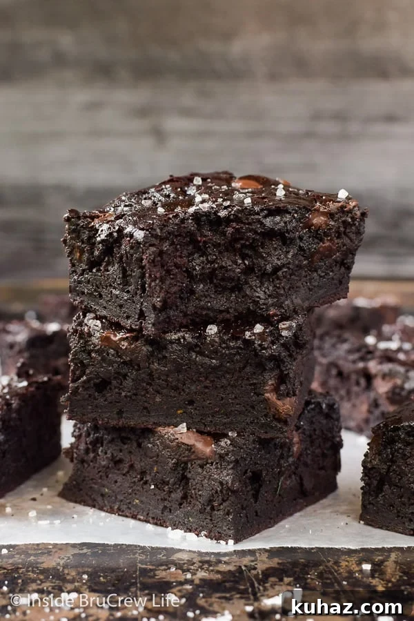 Fudgy Dark Chocolate Zucchini Brownies - the hidden veggies in these brownies make them so fudgy and delicious. You will never know there is zucchini hiding under all that chocolate! A stack of three dark chocolate zucchini brownies on a try with a bite out of the top one
