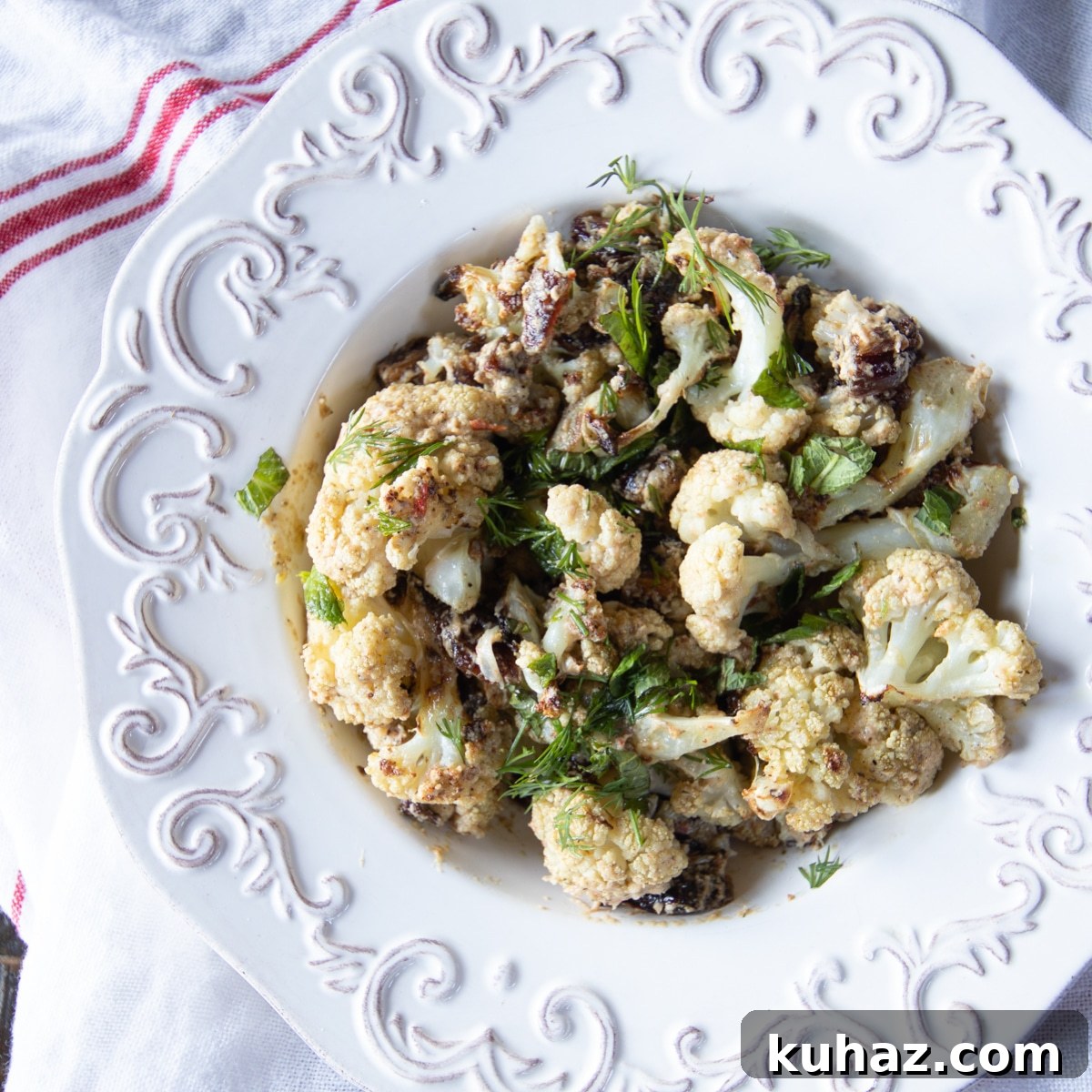 Crispy Roasted Cauliflower with Tahini and Dates 5 Roasted cauliflower tossed in a tahini sauce with dates, topped with mint and dill in a serving bowl.