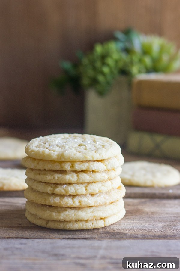 Soft, Chewy Bakery-Style Sugar Cookie Recipe 5 Bakery Style Sugar Cookies in a stack of seven, with more cookies in the background.