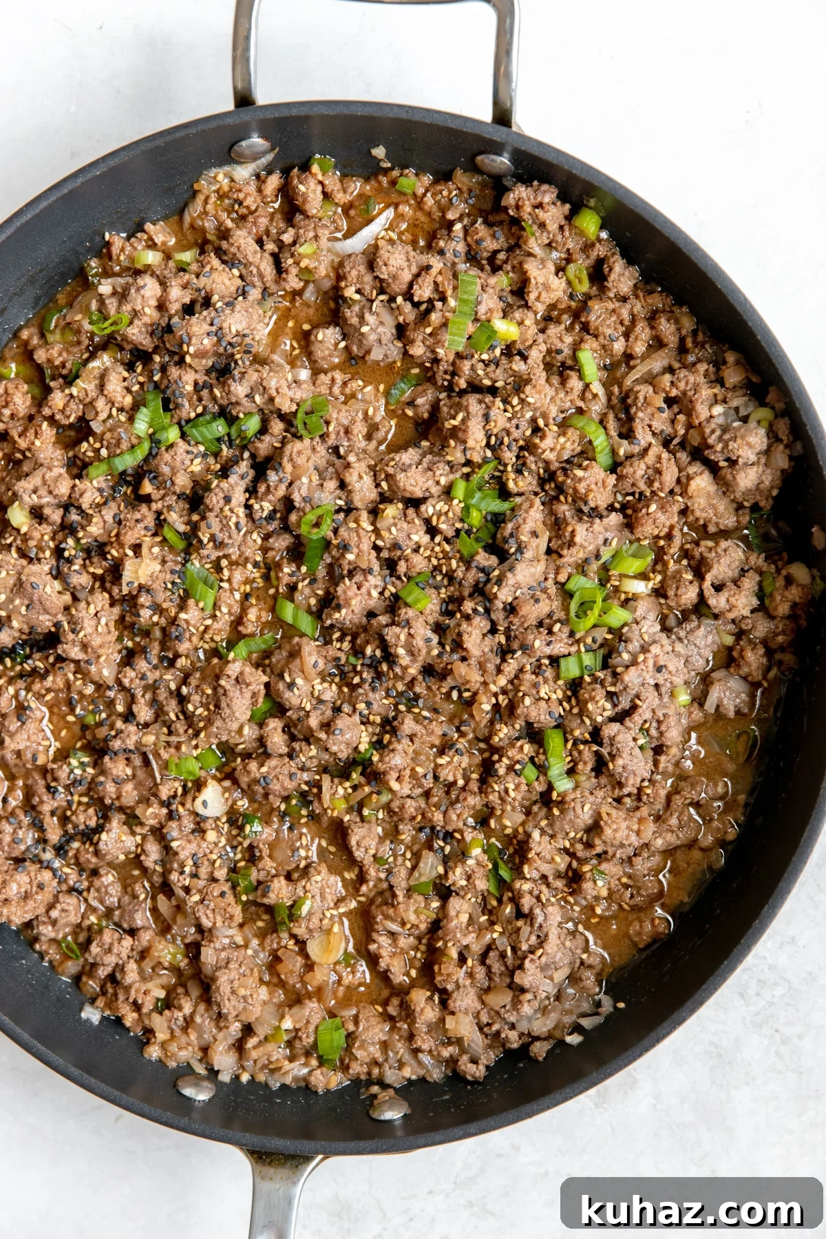 ground beef in a large black skillet with green onions on top