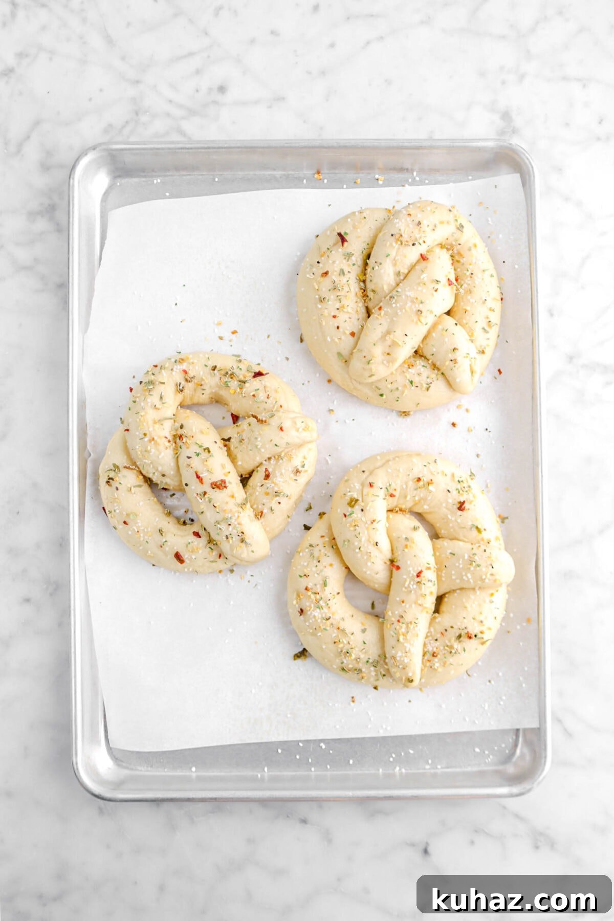 Giant Goat Cheese Stuffed Soft Pretzels 23 three pretzels on lined sheet pan with pretzels salt and herb seasoning on top.