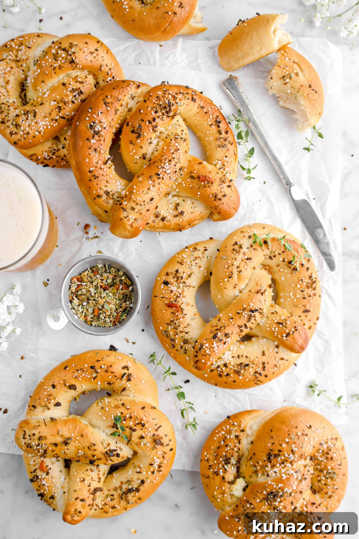 Giant Goat Cheese Stuffed Soft Pretzels 26 overhead shot of pretzels on parchment paper with knife, dried herbs in measuring cup, glass of beer, and flowers beside.