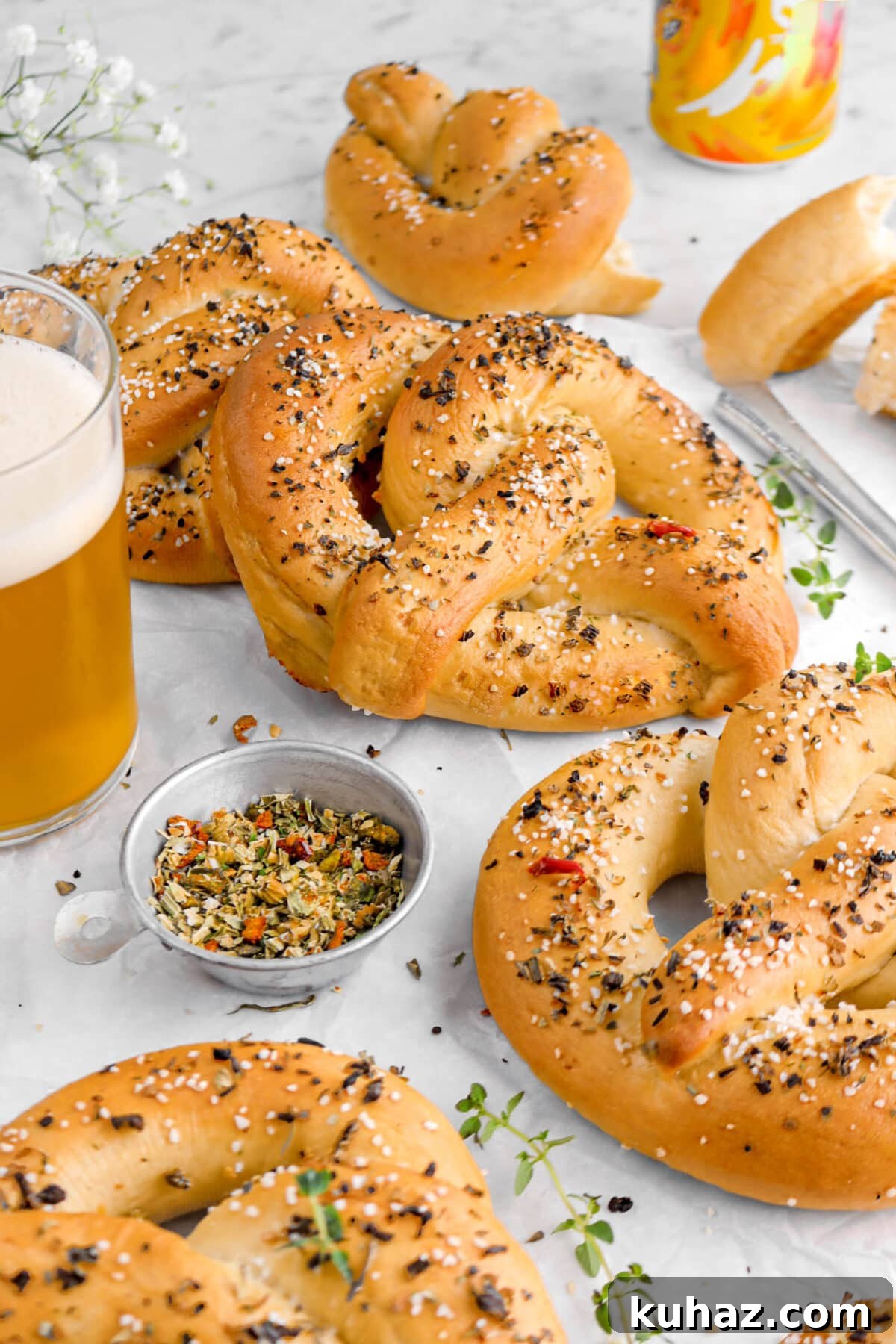 Giant Goat Cheese Stuffed Soft Pretzels 6 front shot of pretzels with two leaning against each other on parchment paper with thyme sprigs around, a measuring cup of spices, and a glass of beer beside.
