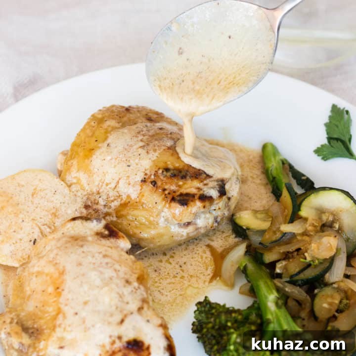 Lemon chicken on a white plate with cooked veggies with a silver spoon drizzling sauce over top.