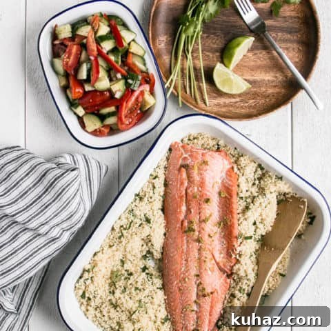 Easy salmon family dinner in a silver backing dish on a white wooden background with towel and veggies around it.