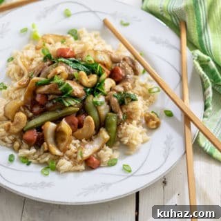 Pork stir fry on a white plate with a green towel and wooden chop sticks by it.