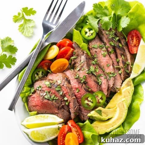 Cooked steak surrounded by lettuce and veggies with a silver spoon and knife by it.