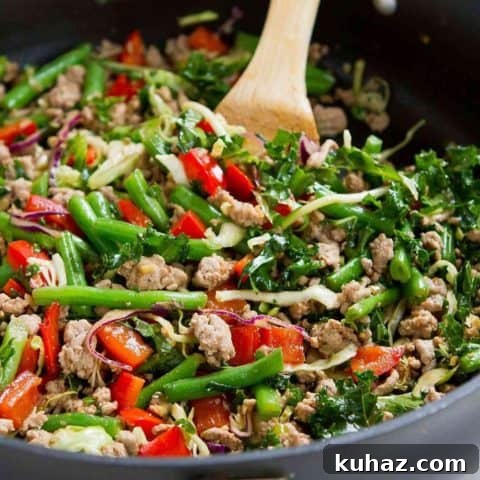 Turkey and veggie stir fry in a large skillet with wooden spoon in it.