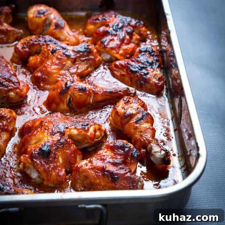 Baked BBQ chicken in a silver baking dish on a dark gray counter.