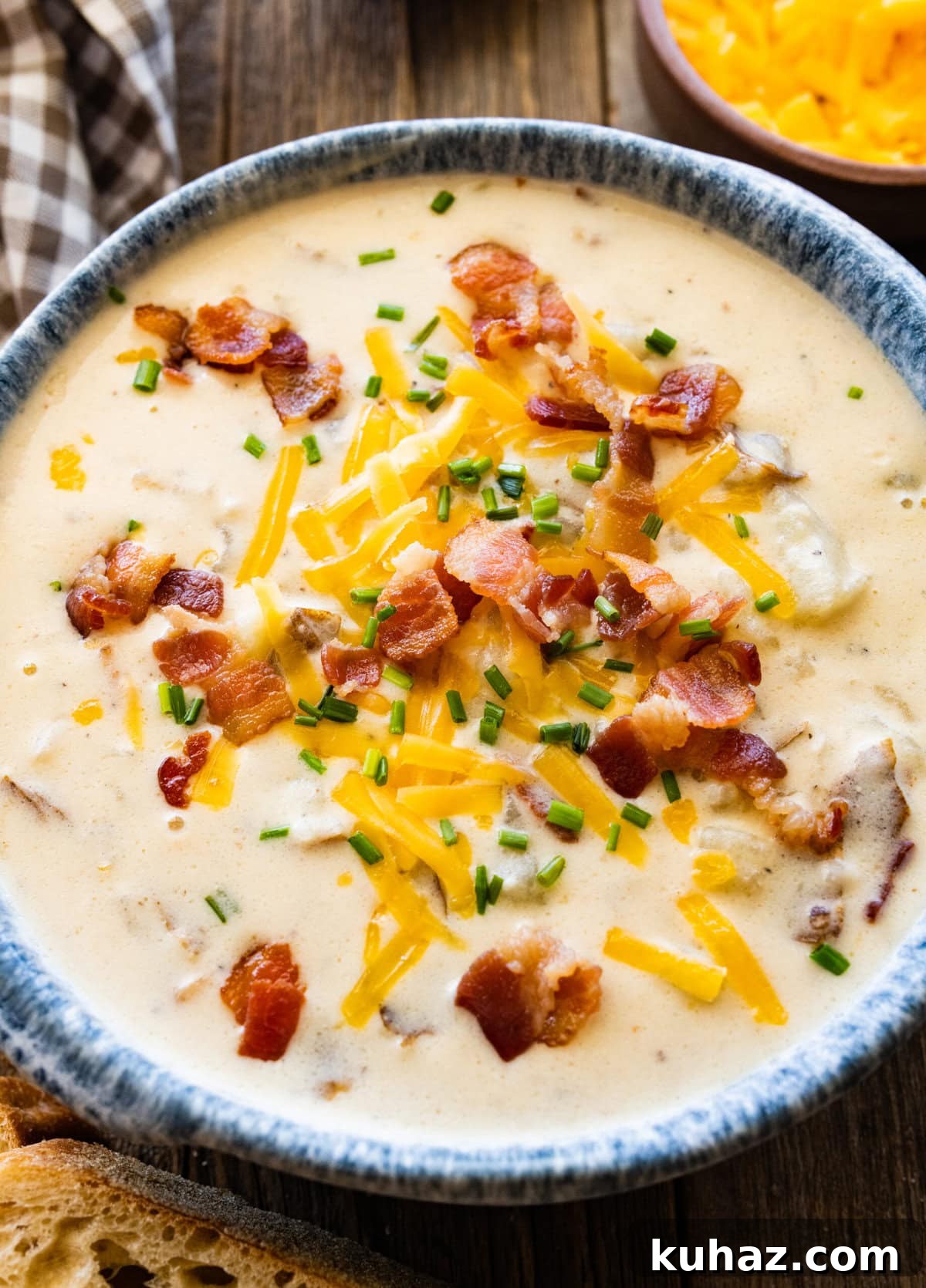Outback Steakhouse Baked Potato Soup Copycat Recipe 15 outback baked potato soup recipe in a bowl with a blue rim. Cheddar cheese and bacon bits on the top. Bread pieces on the side and napkin.