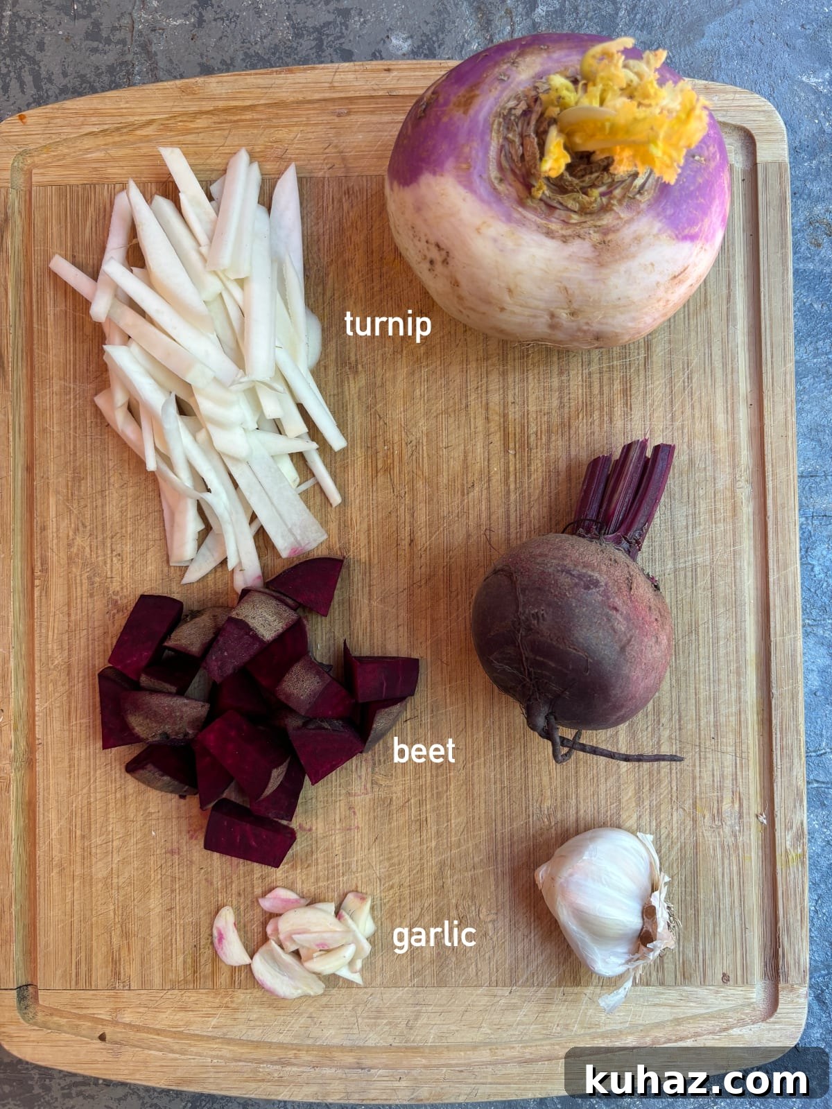 overhead image of a whole turnip next to a sliced turnip, a whole beet next to a diced beet, and a whole garlic clove next to a minced garlic. The ingredients are all together on a wooden cutting board.