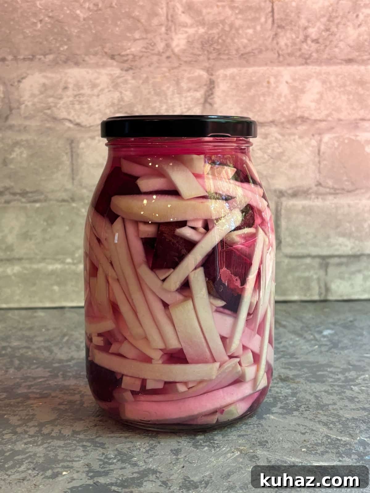 a large glass jar filled with chopped turnips, beets, and garlic covered in brining liquid sealed with a black lid.