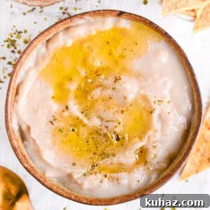 Creamy white bean dip in a bowl, served with a drizzle of olive oil, herbs and baked tortilla chips