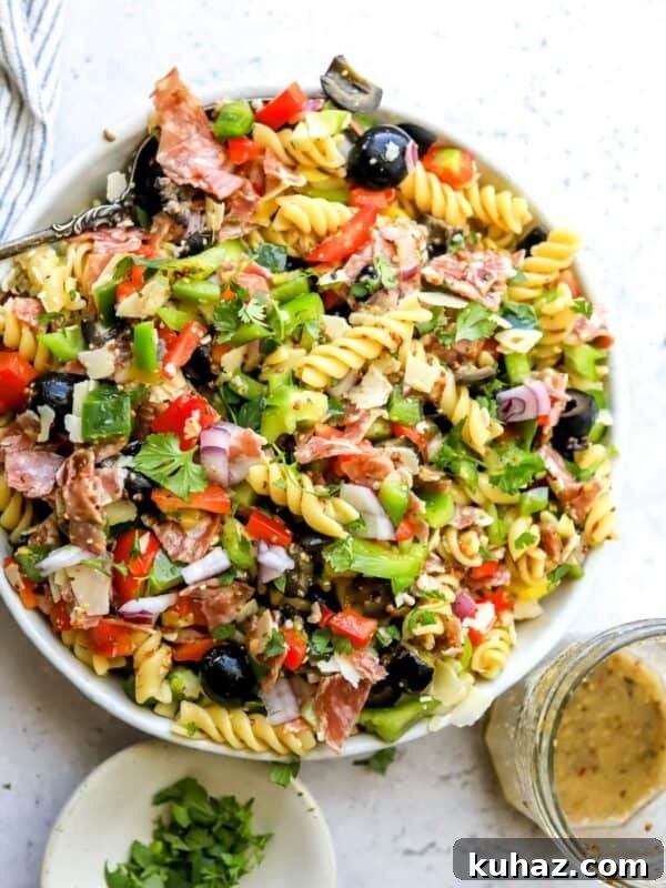 White ceramic bowl with zesty pasta salad in it with Italian dressing on the side. Bowls to the side.
