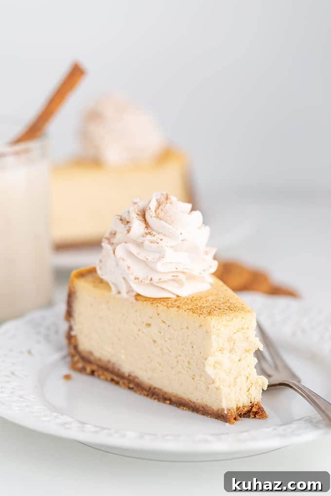 Creamy Eggnog Cheesecake Recipe for the Holidays 6 bite taken out of a cheesecake on a white plate with a fork next to the cheesecake on a white background