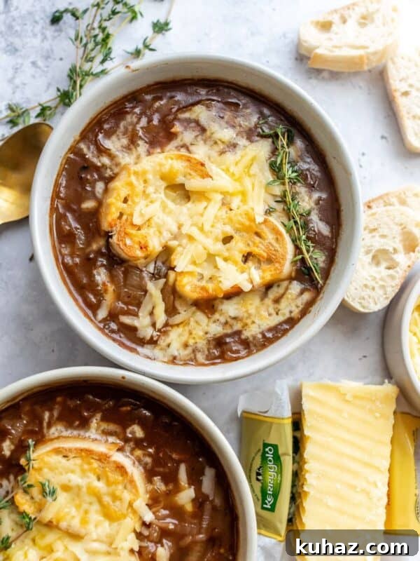Two bowls with healthy french onion soup in them, gold spoons off to the side and cheddar shredded.