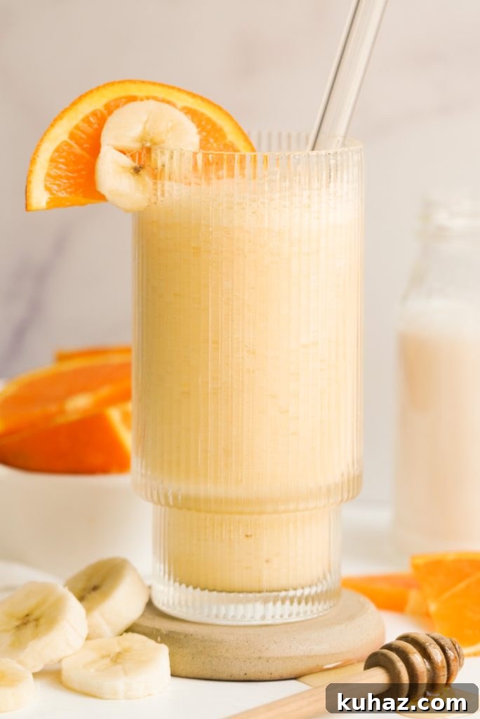 Orange Banana Smoothie Recipe 2 orange banana smoothie in a glass surrounded by banana and orange slices