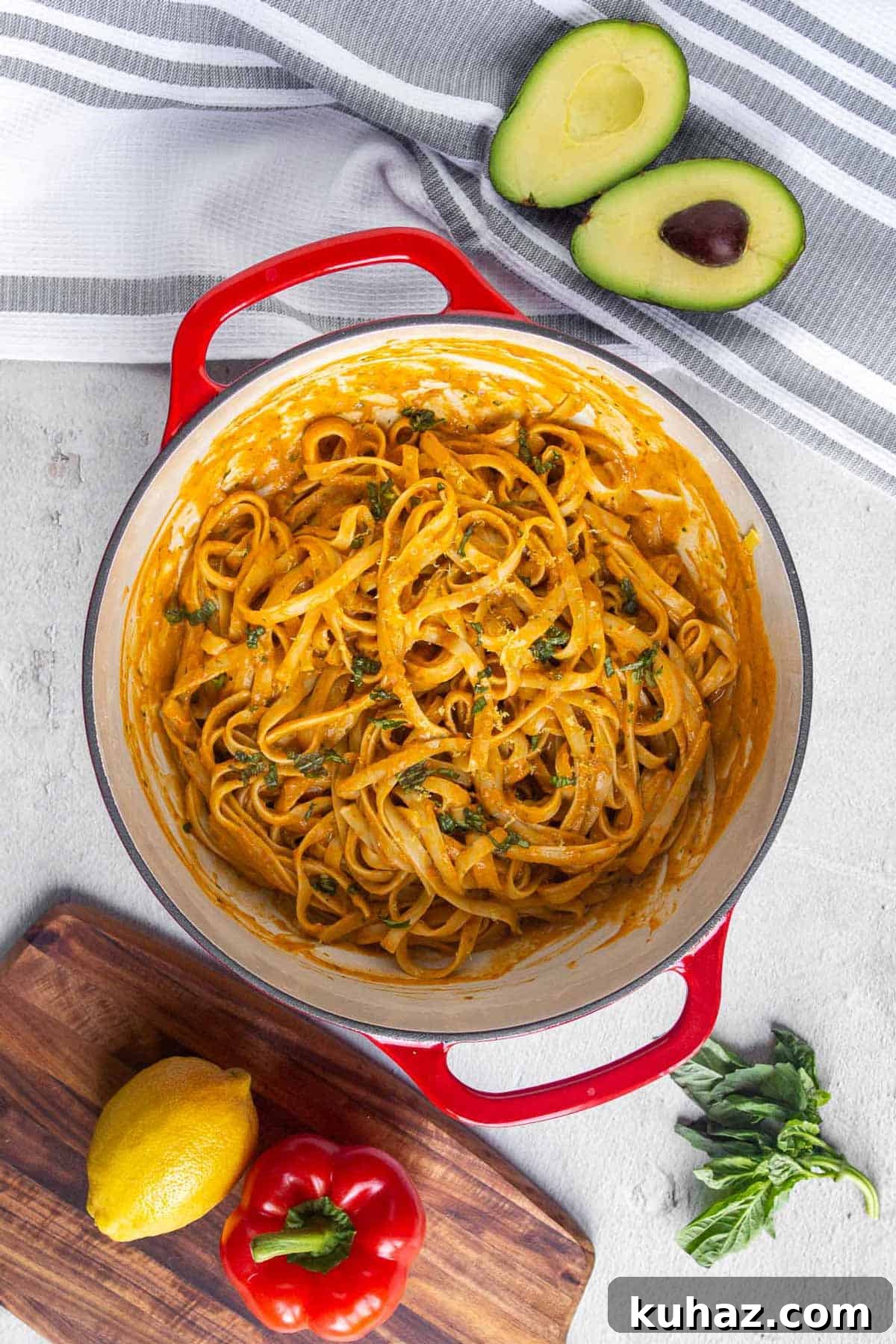 Creamy Avocado Bell Pepper Pasta 8 Top down view of cast iron dutch oven filled with fettuccine coated in creamy roasted red pepper sauce and garnished with fresh basil. The sauce is thick and creamy.