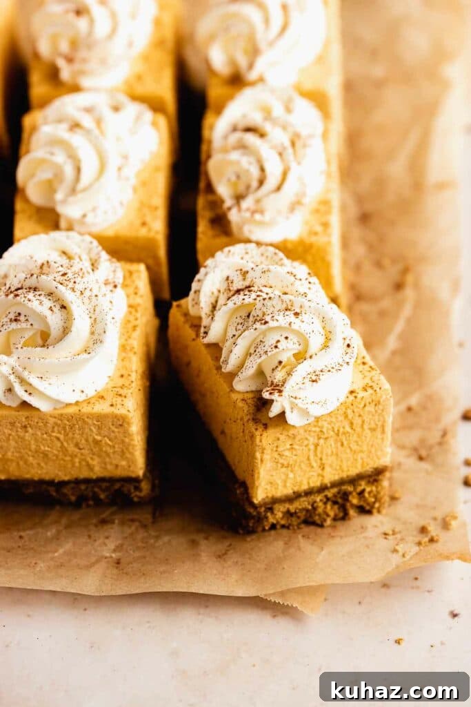 Creamy No-Bake Pumpkin Cheesecake Bars 3 Pumpkin cheesecake bars with whipped cream on parchment paper