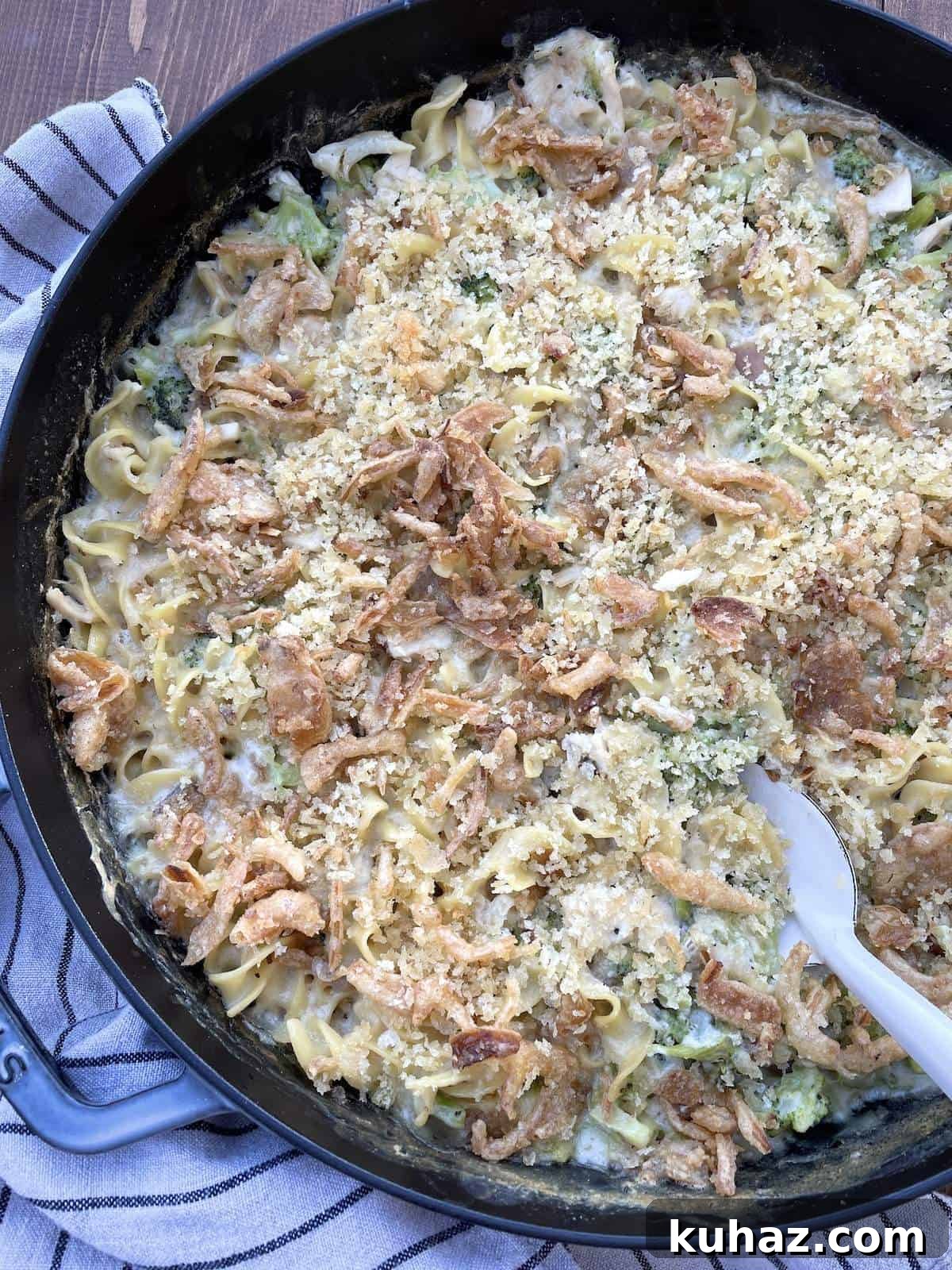 A large cast iron pan filled with cheesy chicken and broccoli noodle casserole with a white serving spoon.