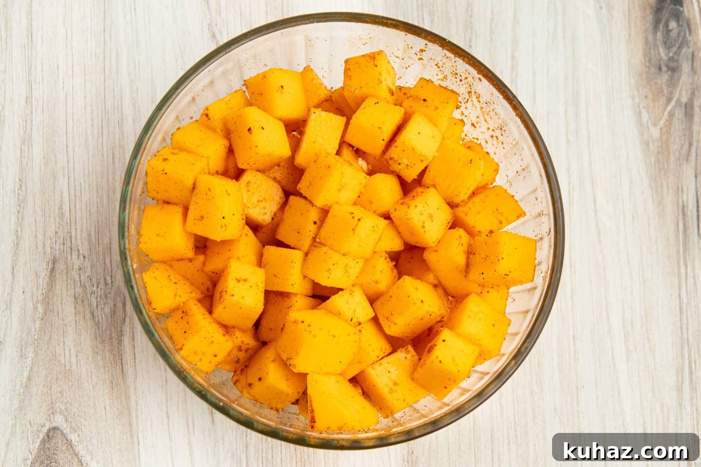 This is a picture of a bowl filled with raw butternut squash mixed with spices.
