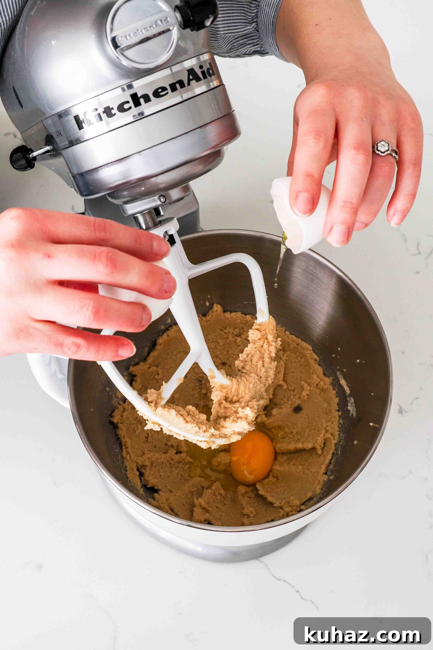 Chewy Double Chocolate Chip Cookies Recipe 6 Two hands crack an egg into creamed butter and sugar in a mixer bowl.