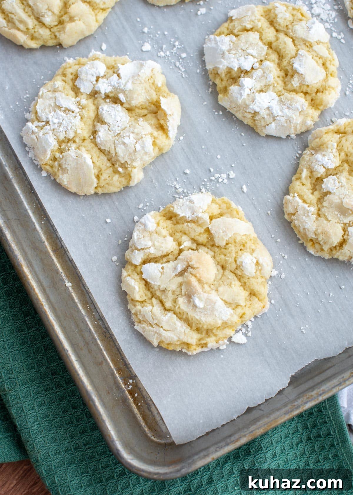 Lemon Crinkle Cookies Made with Sourdough Discard 11 Lemon crinkle cookies coated in powdered sugar baking on a parchment-lined sheet pan, showing cracked tops and soft centers.