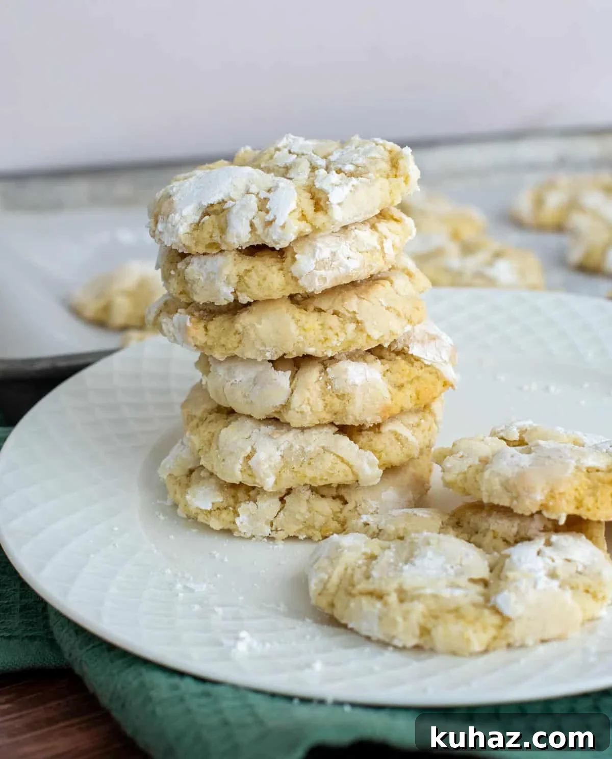 Lemon Crinkle Cookies Made with Sourdough Discard 12 Stack of lemon crinkle cookies made with sourdough discard, coated in powdered sugar with crackled tops on a white plate.