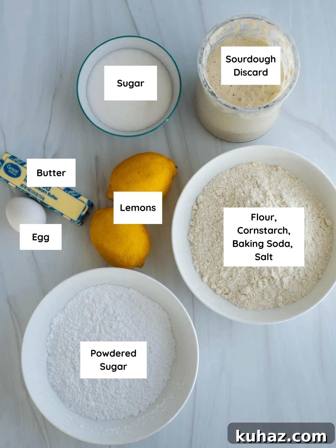 Lemon Crinkle Cookies Made with Sourdough Discard 3 Ingredients for lemon crinkle cookies with sourdough discard including sugar, sourdough discard, flour mixture, powdered sugar, butter, egg, and fresh lemons arranged on a countertop.