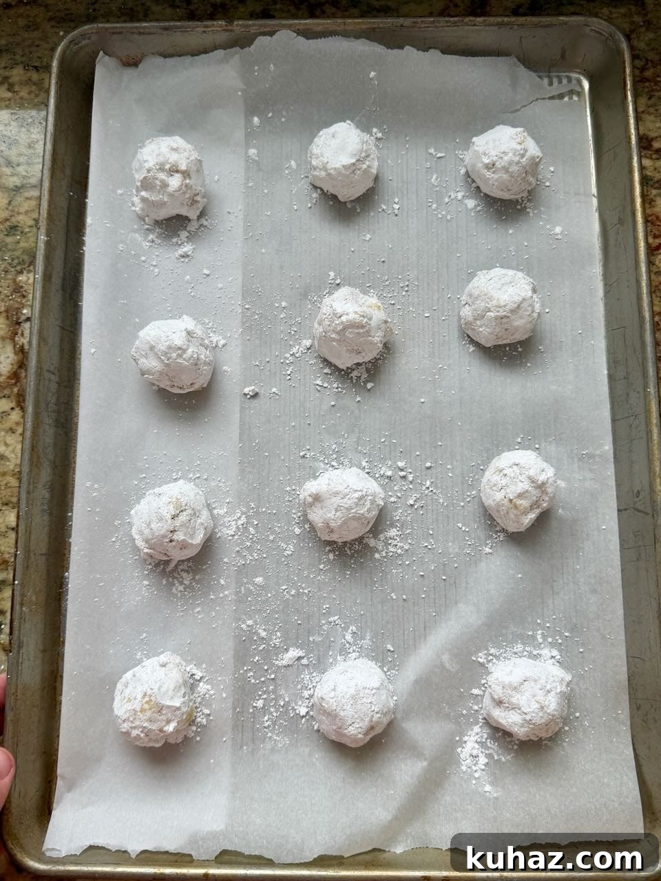 Lemon Crinkle Cookies Made with Sourdough Discard 9 Lemon crinkle cookie dough balls coated in powdered sugar arranged on a parchment-lined baking sheet.