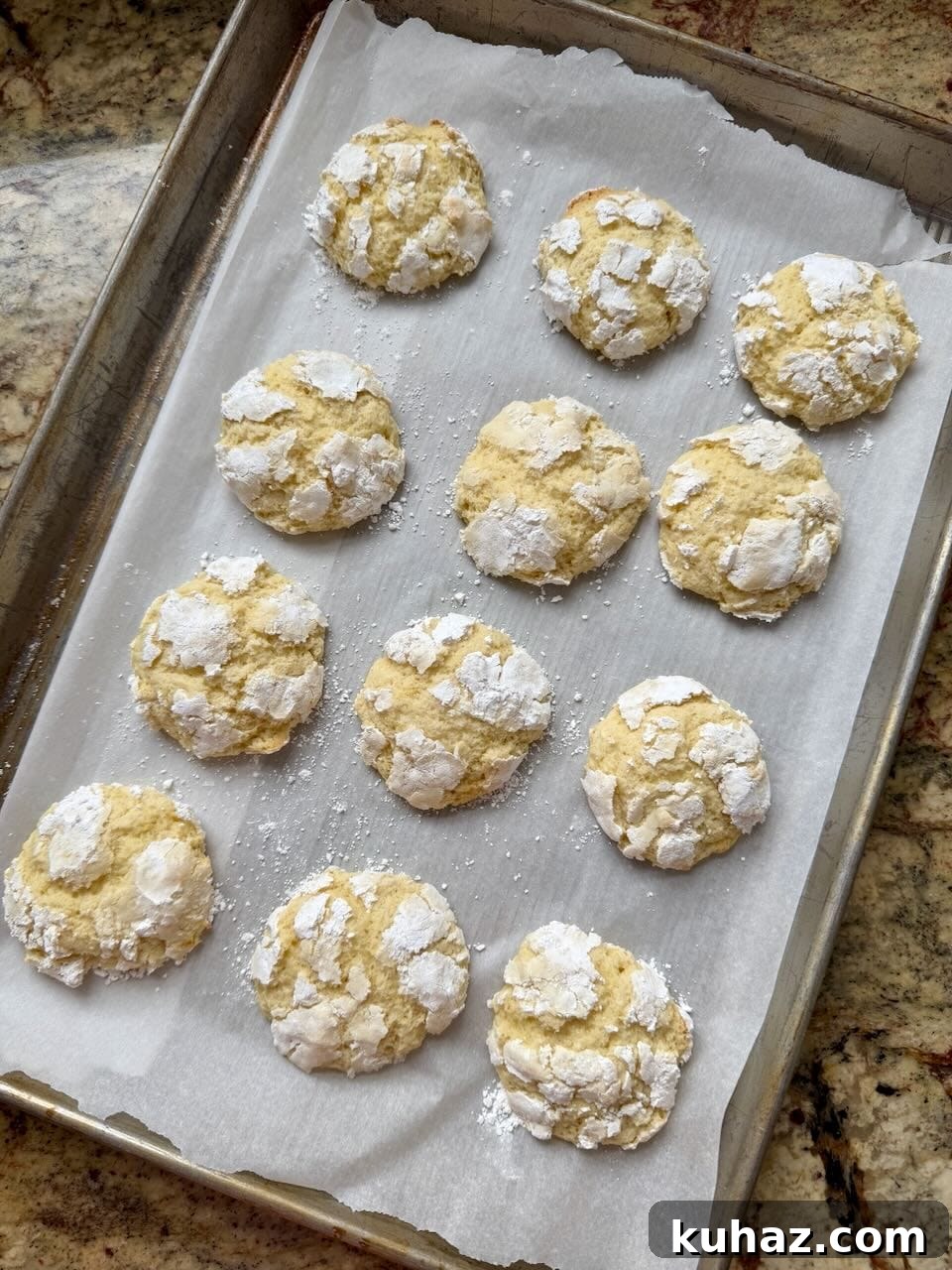 Lemon Crinkle Cookies Made with Sourdough Discard 10 Lemon crinkle cookies coated in powdered sugar baking on a parchment-lined sheet pan, showing cracked tops and soft centers.