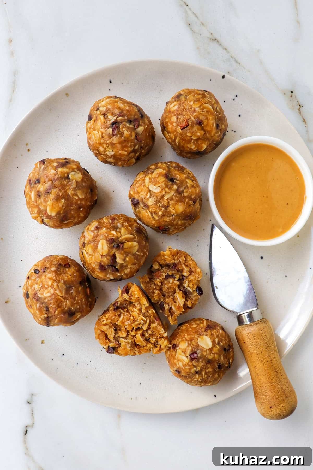No-Bake Peanut Butter Bliss Balls: Protein-Packed Bites 8 Bliss balls on a plate with a knife and dish of peanut butter. One cut in half.