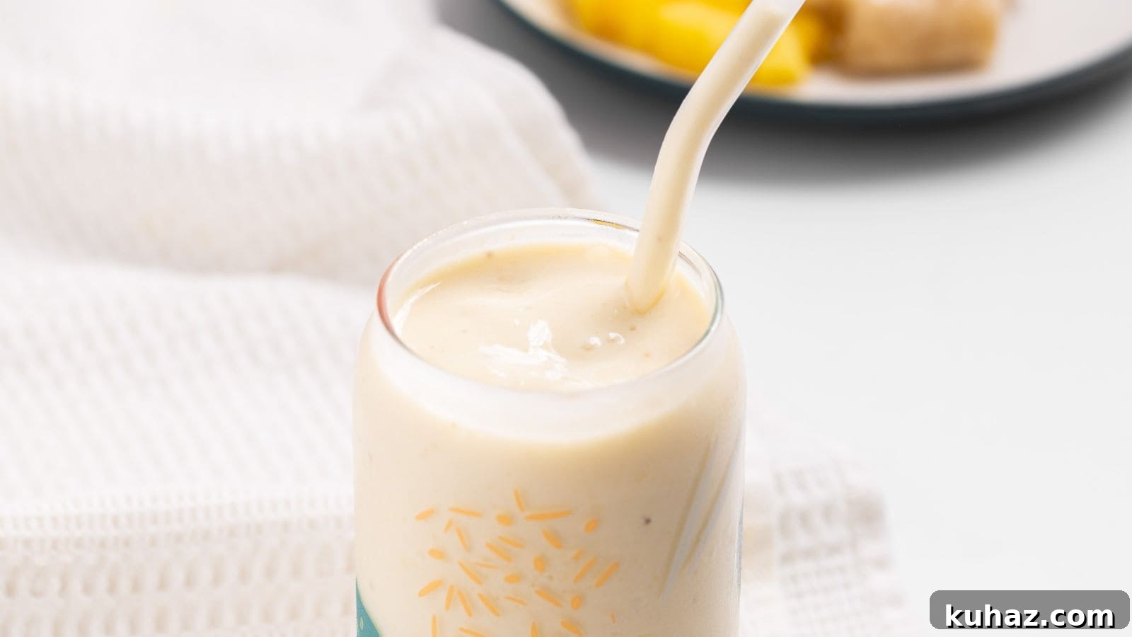 13 Gluten-Free Breakfast Recipes to Kickstart Your Morning 15 A close-up of a pineapple banana smoothie in a glass with a straw, surrounded by a white napkin with pineapple and banana in the background.