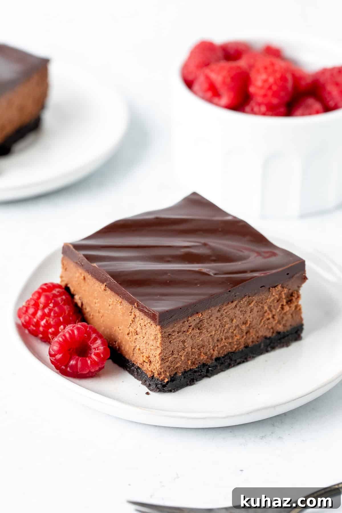 Chocolate Cheesecake Bars Recipe 9 Chocolate cheesecake bar topped with chocolate ganache on a plate, with raspberries