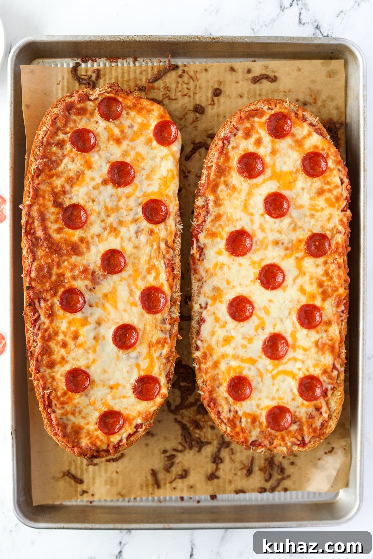 Homemade French Bread Pizza Recipe 8 Two halves of French Bread pizza on a baking sheet.